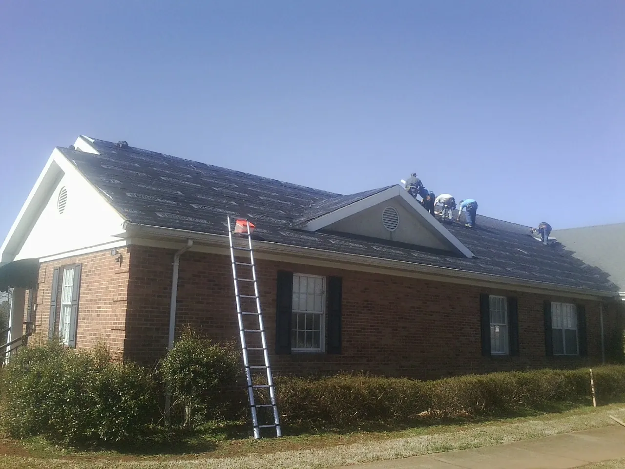 Crew tearing shingles off a brick ranch roof with a ladder set — Metal Roof Repair work by our crew in Clarksville