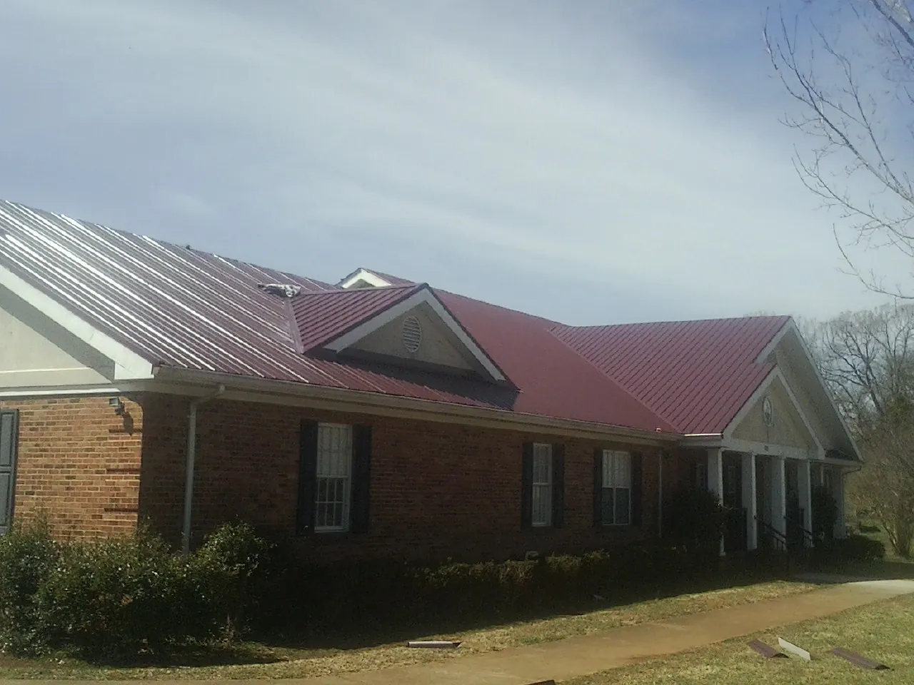 Red metal roof with gabled entries on a long brick building, from a Hail Damage Roof Repair job in Clarksville
