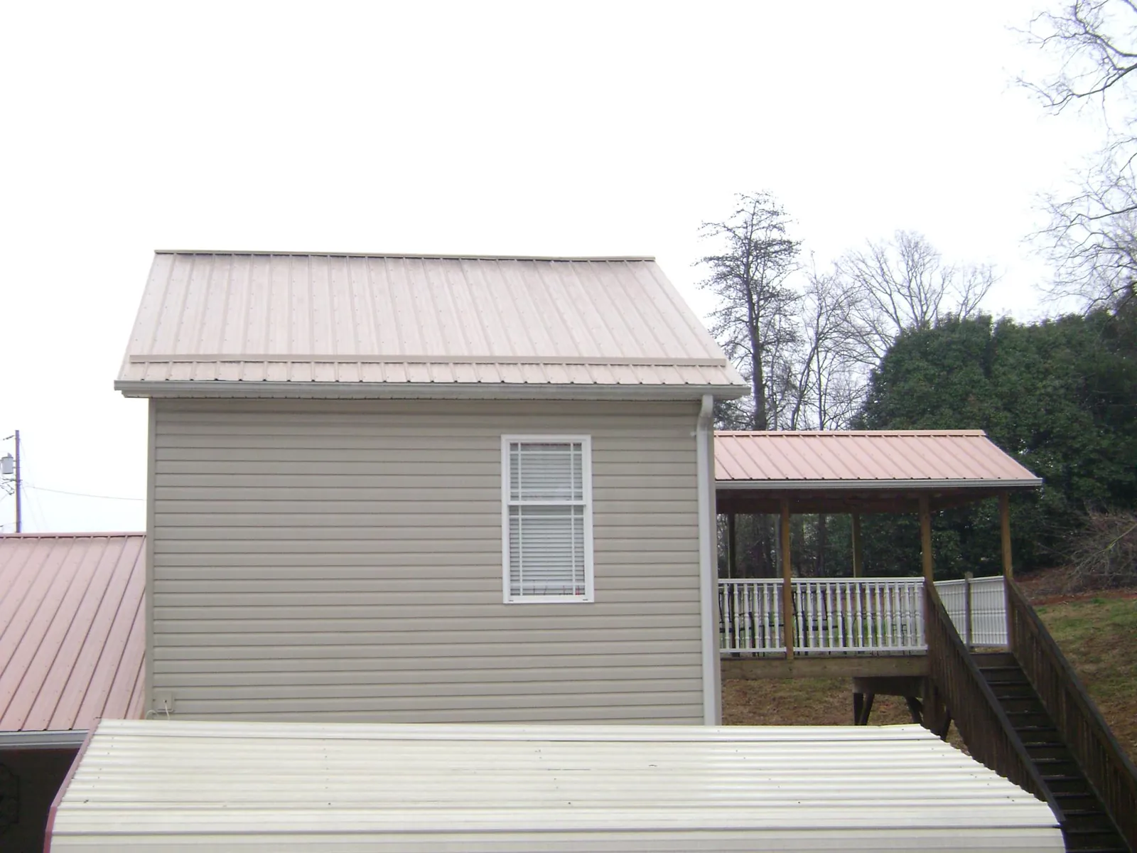 Tan metal roofs on a two story addition and attached porch, from a Roof Replacement job in Clarksville